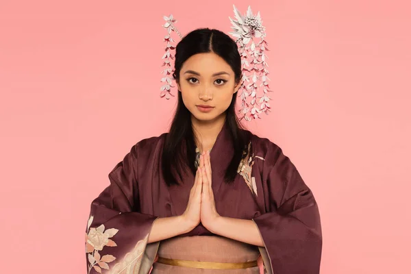 Mulher asiática em quimono com as mãos orando olhando para a câmera isolada em rosa — Fotografia de Stock
