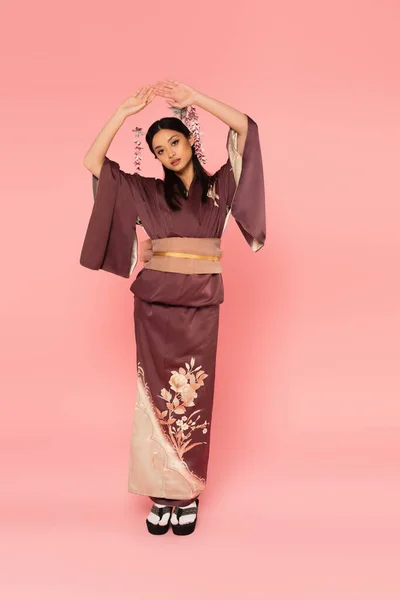Volle Länge der asiatischen Frau in orientalischen Schuhen und Kimono auf rosa Hintergrund — Stockfoto