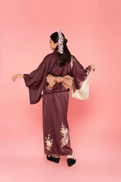 Vista laterale di donna asiatica in posa in kimono tradizionale su sfondo rosa — Foto stock