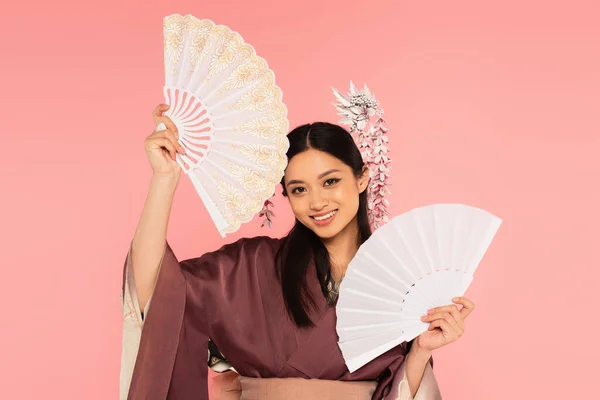 Sorridente donna asiatica che tiene i fan isolati sul rosa — Foto stock