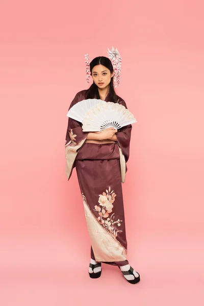 Mulher asiática bonita em roupas tradicionais segurando fãs no fundo rosa — Fotografia de Stock
