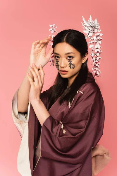 Japanese woman in oriental clothes and hieroglyphs on face isolated on pink — Stock Photo