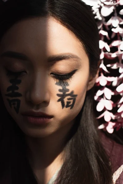 Hieroglyphs on face of young asian woman in light isolated on black — Stock Photo