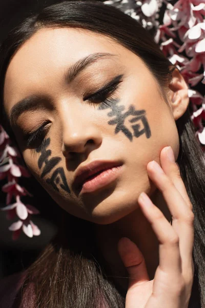 Retrato de mujer asiática con jeroglíficos en la cara y kanzashi aislado en negro - foto de stock