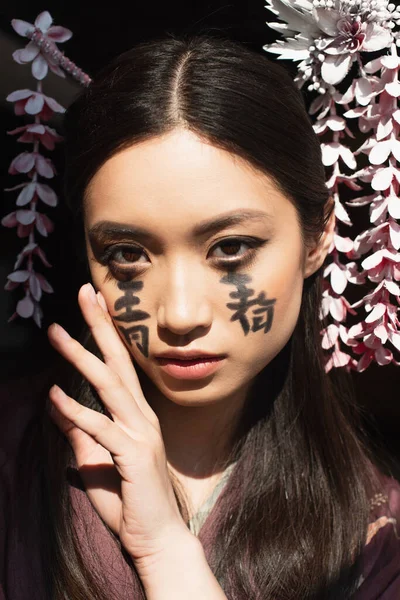 Досить азіатська жінка з ієрогліфами на обличчі і волосками ізольовані на чорному — стокове фото