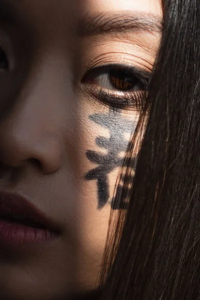 Vue rapprochée de la femme japonaise avec des hiéroglyphes sur le visage à la lumière — Photo de stock