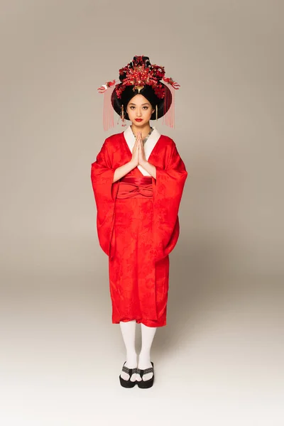 Femme asiatique en vêtements traditionnels debout avec des mains priantes sur fond gris — Photo de stock