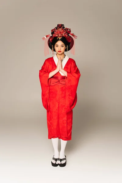 Asian woman in traditional clothes standing with praying hands on grey background — Stock Photo