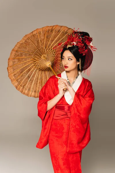 Femme asiatique en kimono rouge exploitation parapluie isolé sur gris — Photo de stock
