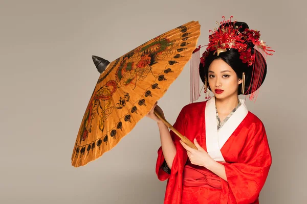 Красивая японка в восточной одежде держит бумажный зонтик изолированный на сером — стоковое фото
