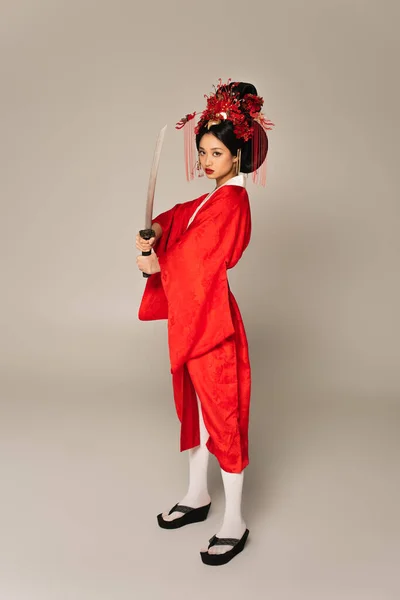 Full length of asian woman holding sword on grey background — Stock Photo