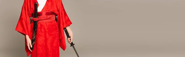 Обрізаний вид жінки в східному одязі, що тримає меч ізольовано на сірому, банер — стокове фото