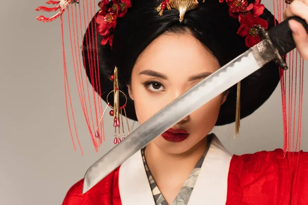 Japanese woman in national costume holding blurred sword near face isolated on grey — Stock Photo