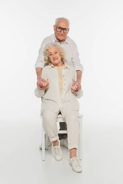 Happy elderly man holding hands with wife sitting on chair on white — Stock Photo