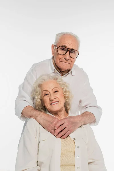 Elderly man hugging smiling wife with hands on breast isolated on white — Stock Photo