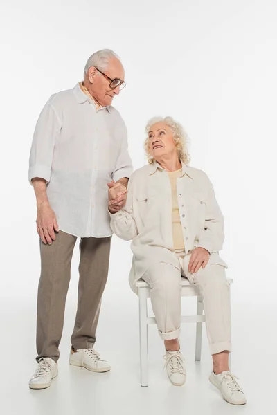 Happy elderly man holding hand of wife sitting on chair on white — Stock Photo