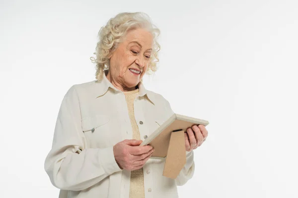 Donna anziana sorridente in camicetta e camicia tenendo cornice foto in mani isolate su bianco — Foto stock