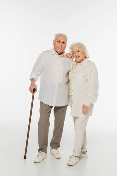 Elderly woman standing with husband holding walking stick on white — Stock Photo