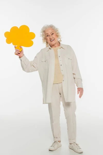 Lächelnde ältere Frau in legerer Kleidung mit gelber Gedankenblase in der Hand auf weißem Grund — Stockfoto