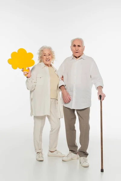 Smiling elderly woman holding yellow thought bubble near husband with walking stick on white — Stock Photo