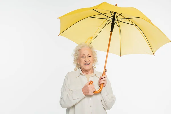 Lächelnde ältere Frau in legerer Kleidung mit gelbem Regenschirm auf weißem Hintergrund — Stockfoto