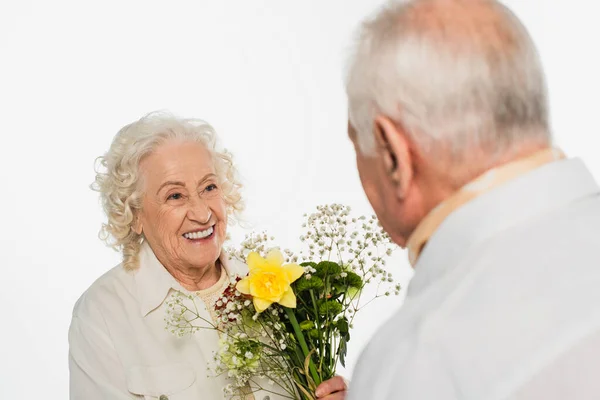 Пожилой мужчина, дарящий букет цветов улыбающейся жене, изолированной на белом — стоковое фото