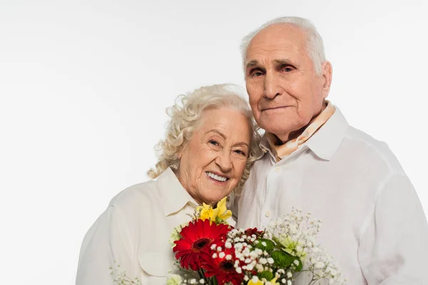 Щаслива літня пара тримає букет квітів і дивиться на камеру ізольовано на білому — стокове фото