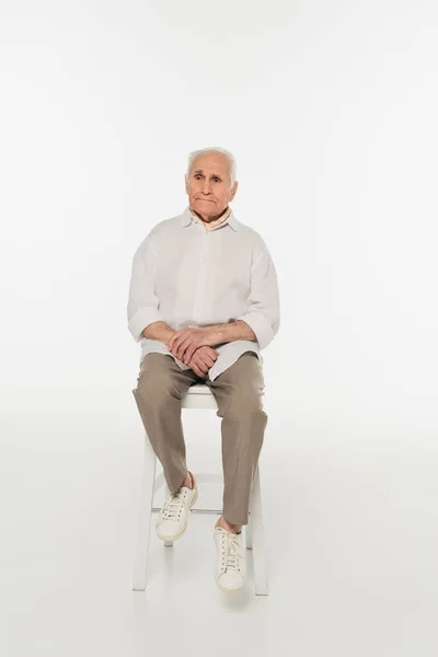 Sad elderly man in casual clothes sitting on stool on white — Stock Photo