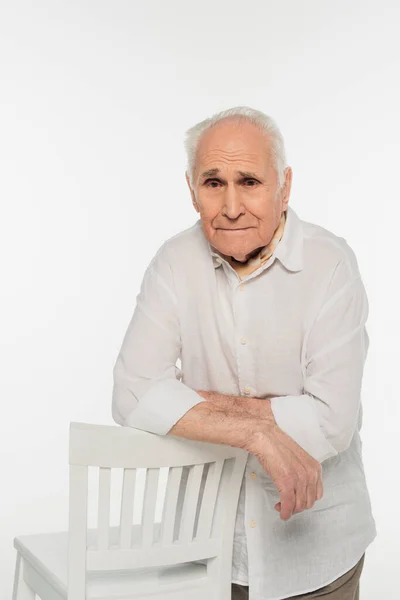 Aufgebrachter älterer Mann in legerer Kleidung, der neben einem Hocker steht und isoliert auf weiß in die Kamera schaut — Stockfoto