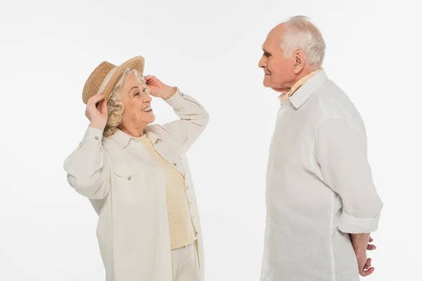 Mujer anciana positiva ajustando sombrero en la cabeza y mirando marido aislado en blanco - foto de stock