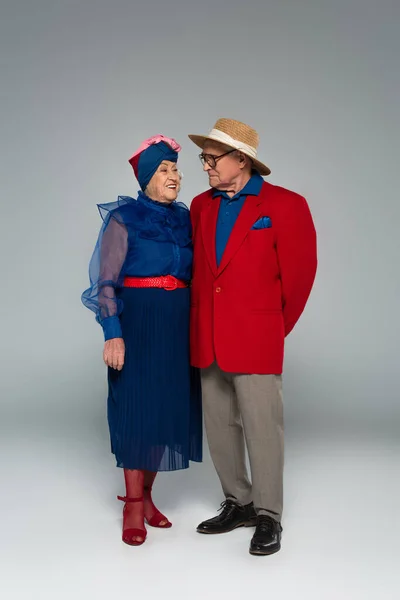Sonriente pareja de ancianos en ropa elegante de pie en gris — Stock Photo