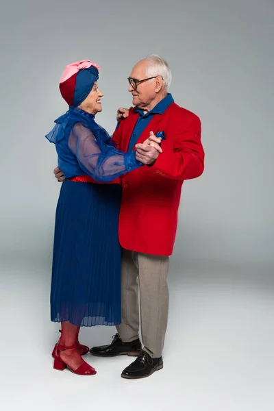 Glückliches älteres Paar in stilvoller Kleidung tanzt auf grau — Stockfoto