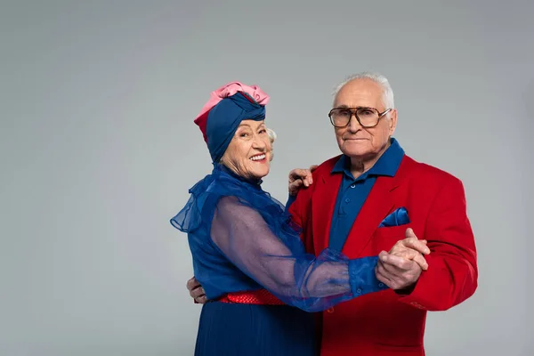 Sonriente pareja de ancianos en vestido azul y chaqueta roja bailando aislados en gris - foto de stock