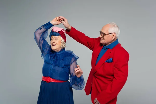 Sonriente pareja de ancianos en vestido azul y chaqueta roja bailando aislados en gris - foto de stock