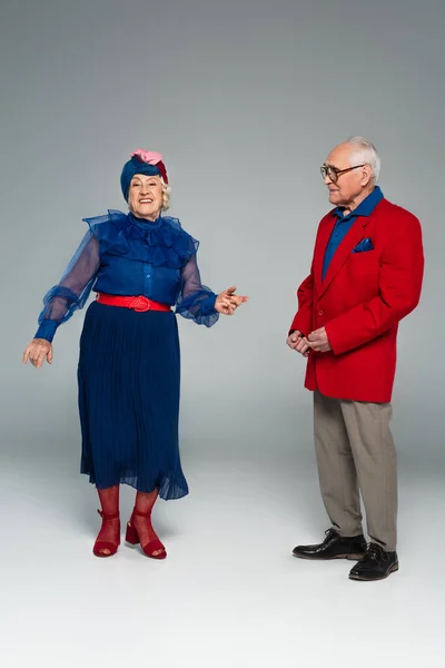 Couple âgé souriant en robe bleue et blazer rouge dansant sur gris — Photo de stock