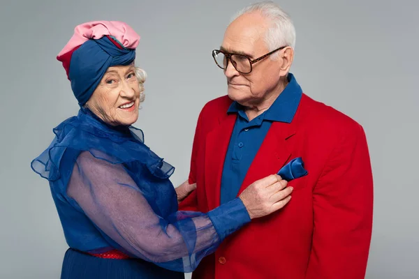 Feliz casal idoso em vestido azul e blazer vermelho abraçando isolado no cinza — Fotografia de Stock