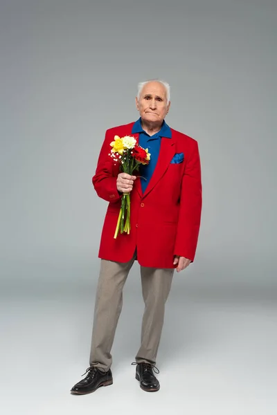 Uomo anziano in abiti eleganti in piedi con mazzo di fiori su grigio — Foto stock