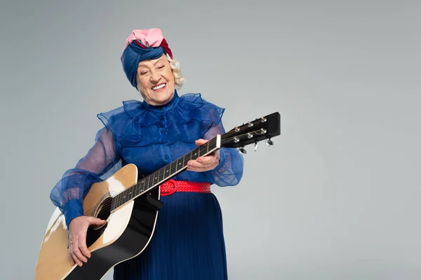 Smiling elderly woman in stylish clothes holding acoustic guitar isolated on grey — Stock Photo