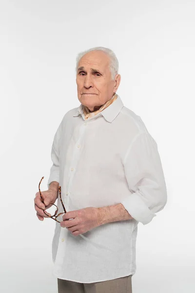 Homme âgé souriant en vêtements décontractés tenant des lunettes dans les mains isolées sur blanc — Photo de stock