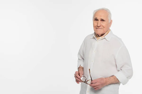 Улыбающийся пожилой мужчина, держащий очки и смотрящий на камеру, изолированную на белом — стоковое фото