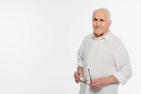 Sorridente uomo anziano tenendo gli occhiali e guardando la fotocamera isolata su bianco — Foto stock