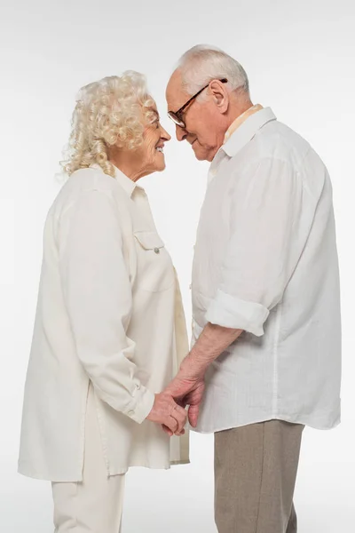 Happy elderly couple in casual clothes standing with holding hands and looking at each other isolated on white — Stock Photo