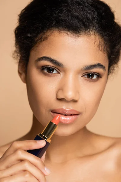 Close up of african american woman applying lipstick isolated on beige — Stock Photo