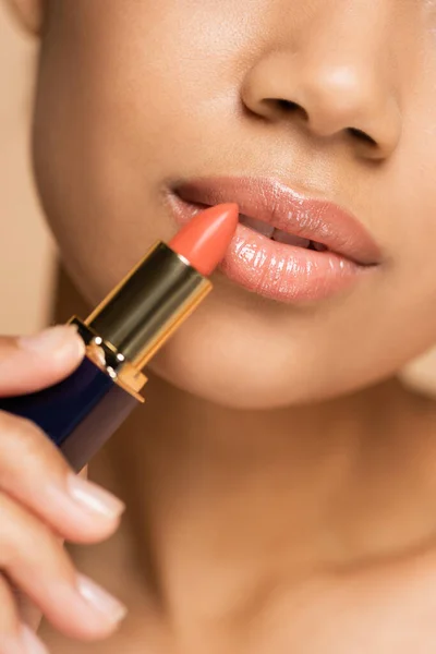 Vista recortada de mujer afroamericana aplicando lápiz labial aislado en beige - foto de stock