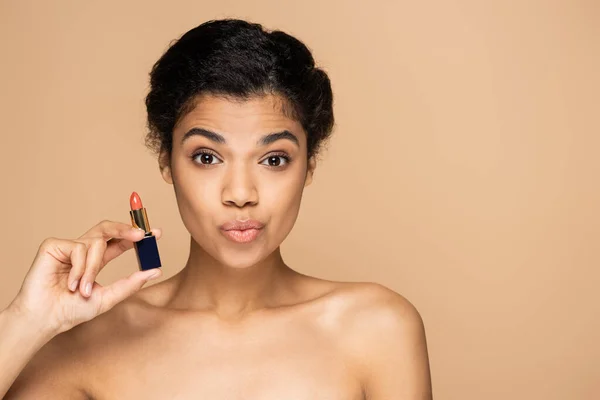 Afroamerikanerin schmollt Lippen und hält Lippenstift isoliert auf beige — Stockfoto