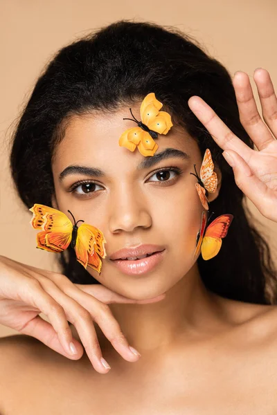 Afrikanisch-amerikanische Frau mit orangefarbenen Schmetterlingen im Gesicht, die isoliert auf beige in die Kamera blickt — Stockfoto