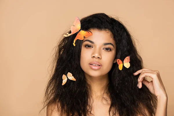 Mujer joven afroamericana con mariposas naranjas en el pelo aislado en beige - foto de stock