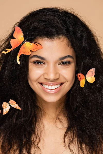 Morena mujer afroamericana con mariposas naranjas en el pelo aislado en beige - foto de stock