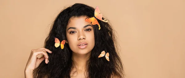 Jeune femme afro-américaine aux papillons orange sur cheveux isolés sur beige, bannière — Photo de stock