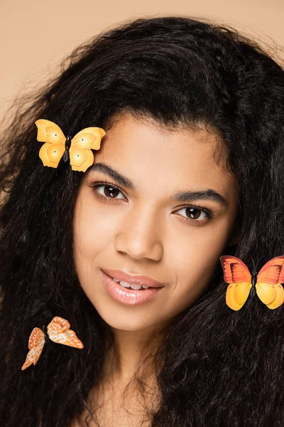 Close up de jovem afro-americana com borboletas laranja no cabelo perto do rosto isolado no bege — Fotografia de Stock